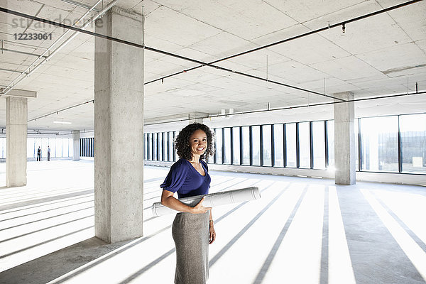 Schwarze Architektin  die in einem großen leeren  rohen Büroraum steht.