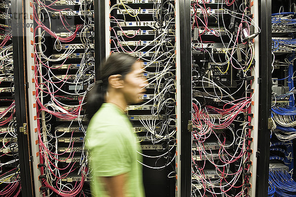 Asiatisch-amerikanischer männlicher Techniker  der an einem CAT 5-Kabelbündelungssystem in einem großen Computer-Serverraum arbeitet.