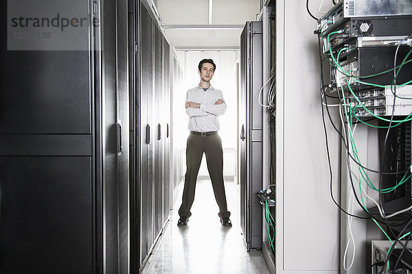 Ein männlicher Computertechniker  der in einem Gang mit Serverschränken in einer Computer-Serverfarm steht