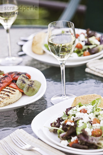 Nahaufnahme eines Glases Wein und einer gesunden Mahlzeit mit Salat auf einem Tisch.