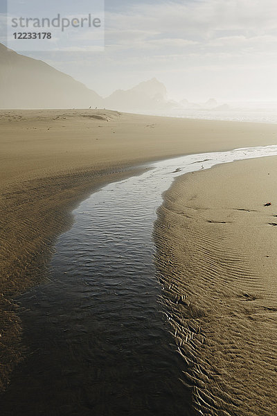 Kleine Bucht am Sandstrand in der Nähe des Ozeans in der Abenddämmerung  Felsen und Klippen in der Ferne.