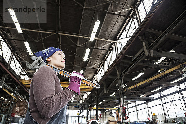 Schwarze Fabrikarbeiterin  die in einer Blechfabrik einen großen Schraubenschlüssel hält.