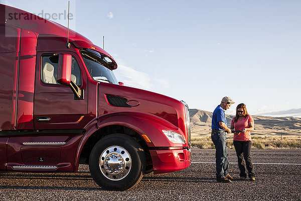 Das Fahrerteam aus Ehemann und Ehefrau prüft ihre Reiseroute  während sie vor ihrem Lastwagen stehen.