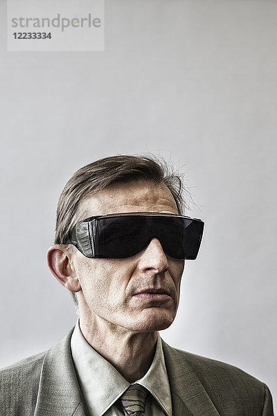 Studioporträt eines kaukasischen männlichen Schauspielers  der eine große Sonnenbrille oder eine Schutzbrille mit abgedunkelten Gläsern trägt.