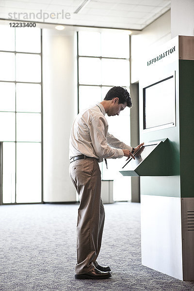 Geschäftsmann an einem Informationskiosk in einem großen Lobbybereich.
