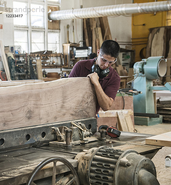 Kaukasischer Fabrikarbeiter  der in einer holzverarbeitenden Fabrik eine große Holzplatte schneidet.