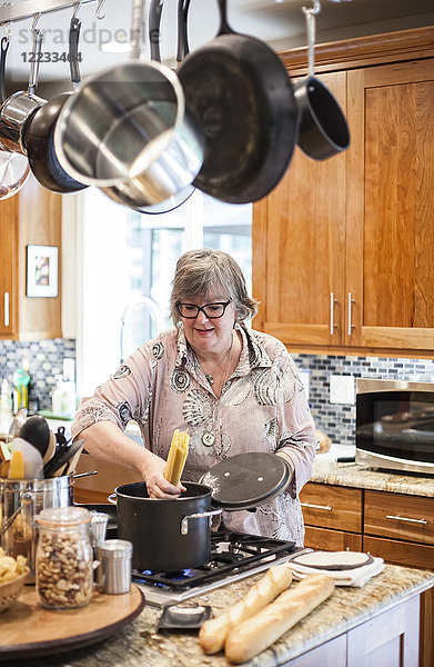 Ältere Frau  die überprüft  ob ein Topf mit Nudeln in der heimischen Küche richtig kocht.