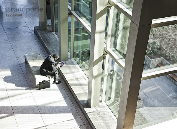 Schwarzer Geschäftsmann auf einem Notebook-Computer  der im Wartebereich einer großen offenen Lobby sitzt.
