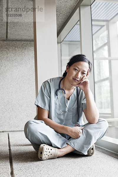 Asiatische Ärztin in OP-Kleidung in einem Krankenhausflur.