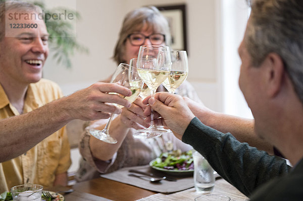 Seniorenpaare stoßen auf eine Dinnerparty zu Hause mit Gläsern Weißwein an.
