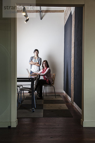 Kaukasierin und Asiatin arbeiten an einem Laptop-Computer in einem kleinen Konferenzraum.