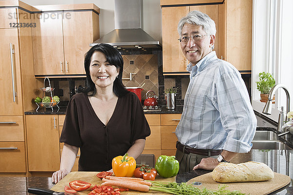 Asiatischer Mann und Frau  die in ihrer Küche frisches Gemüse zubereiten.