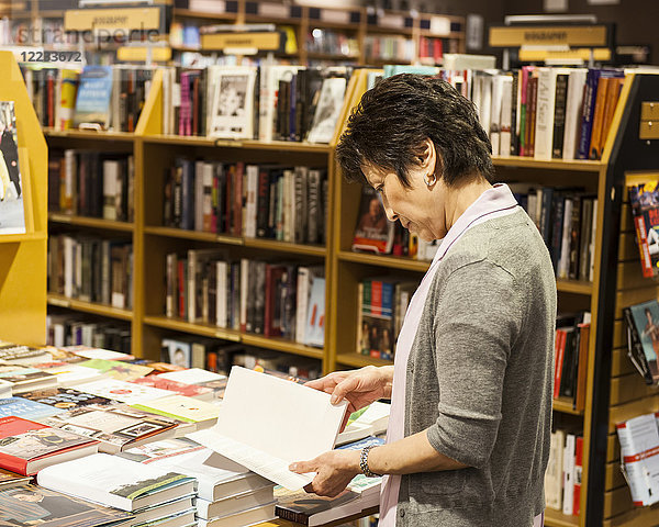 Asiatisch-amerikanische Frau blättert in einer Buchhandlung durch Bücher.