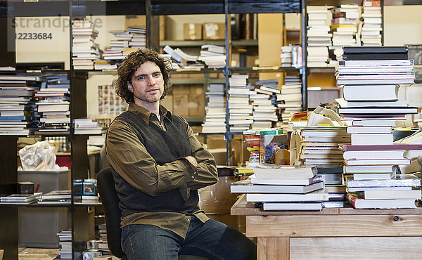 Porträt eines kaukasischen männlichen Angestellten einer Buchhandlung  der in der Gebrauchtbuchabteilung des Ladens arbeitet.