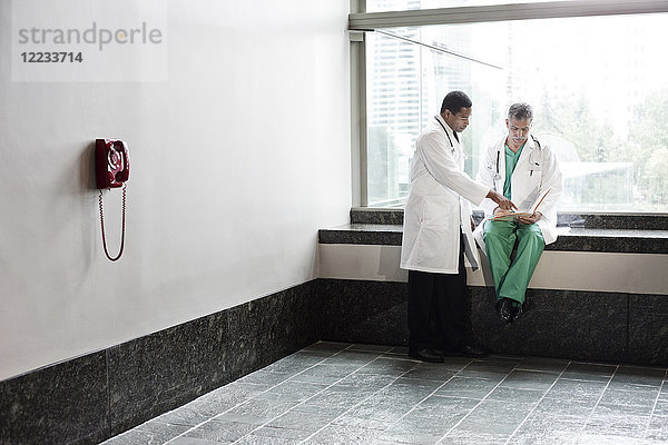 Kaukasische und schwarze Ärzte beraten sich über eine Krankenakte in einem Krankenhausflur.