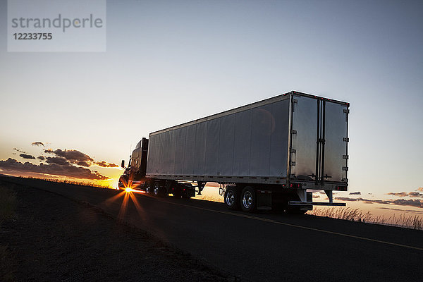Silhouette eines Lastwagens  der bei Sonnenuntergang auf einer Autobahn fährt.