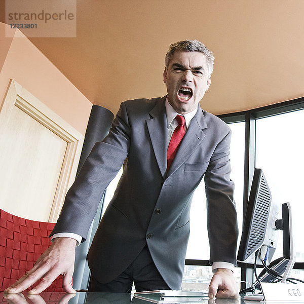 Ein wütender kaukasischer Geschäftsmann in Anzug und Krawatte schreit den Betrachter des Fotos an.