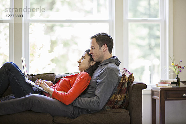Kaukasischer Mann und gemischtrassige kaukasische Frau  die einen Laptop benutzen  während sie zu Hause auf einer Couch sitzen.