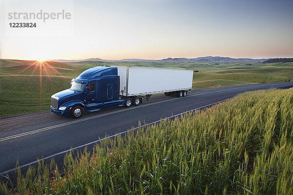 Kommerzieller Lastwagen fährt bei Sonnenuntergang durch Weizenfelder im Osten Washingtons  USA.