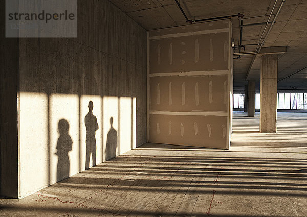 Schatten von Geschäftsleuten werfen sich auf die Rigipswand eines großen leeren  rohen Büroraums.