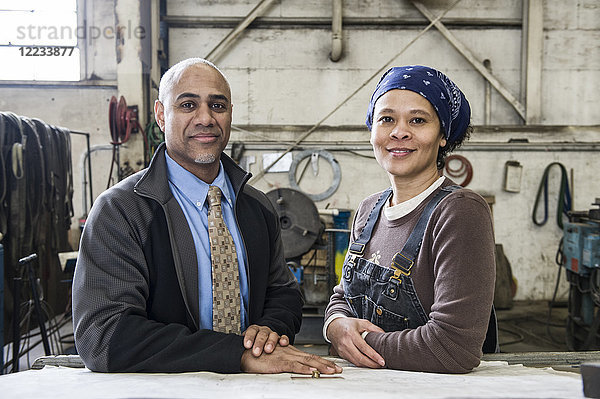 Schwarzer Besitzer einer Blechfabrik und eine schwarze Fabrikarbeiterin besprechen Pläne an einem Arbeitsplatz auf dem Boden der Fabrik.
