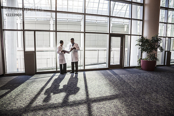 Ärztinnen und Ärzte beraten sich in einer Krankenhauslobby über Krankenakten.