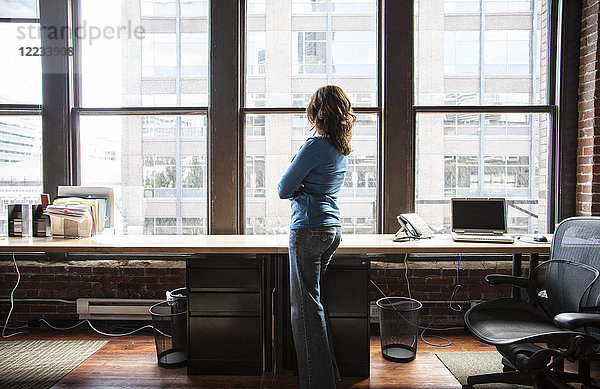 Kaukasische Frau am Büroarbeitsplatz in der Nähe einer großen Fensterbank.