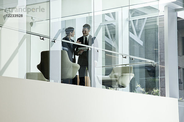 Geschäftsmann und -frau stehen hinter dem Fenster eines Konferenzraums in einem großen Geschäftszentrum.