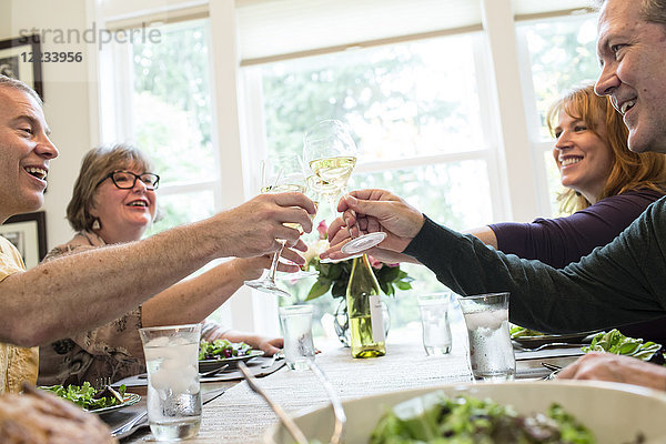 Seniorenpaare stoßen auf eine Dinnerparty zu Hause mit Gläsern Weißwein an.