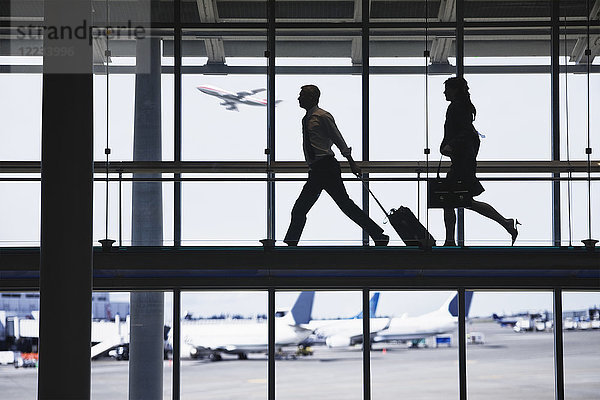 Geschäftsmann und Geschäftsfrau rennen  um auf einem Flughafengehweg ein Flugzeug zu erwischen.