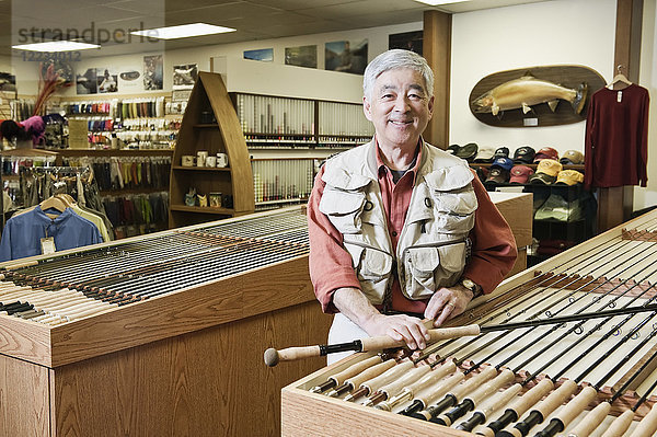 Porträt eines asiatisch-amerikanischen älteren männlichen Besitzers eines Fliegenfischer-Einzelhandelsladens  der eine Fliegenfischerweste trägt.