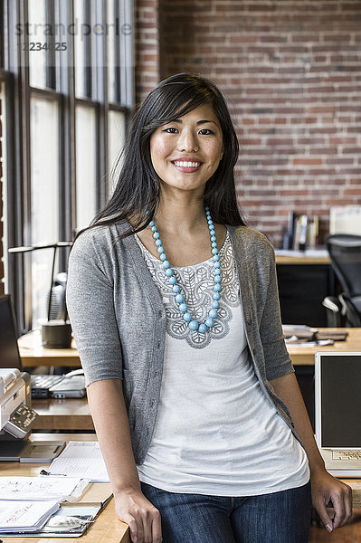 Asiatische Frau an ihrem kreativen Büroarbeitsplatz.