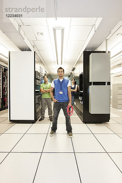 Portrait von drei multiethnischen Technikern  die in einem großen Computer-Serverraum arbeiten.