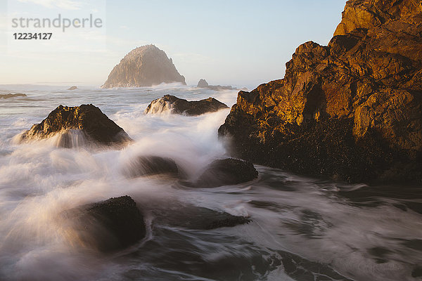Meereslandschaft mit brechenden Wellen über Felsen in der Abenddämmerung.