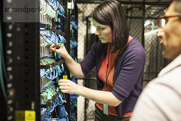 Kaukasische Technikerinnen und Techniker  die in einer großen Computer-Serverfarm an CAT 5-Kabeln arbeiten.