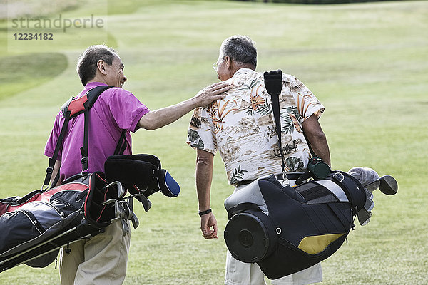 Zwei ältere Freunde spielen Golf und gehen auf einem Fairway auf ihre nächsten Schläge zu.