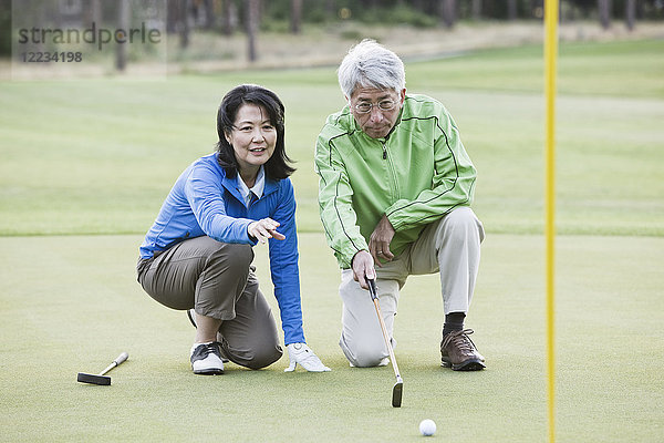 Ein asiatisches Seniorenpaar wirft einen Blick auf die Richtung des nächsten Putts auf dem Grün.