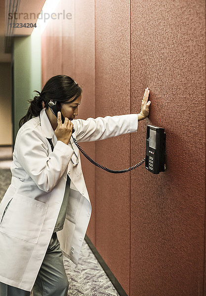 Asiatische Ärztin am Telefon in einer Krankenhauslobby.