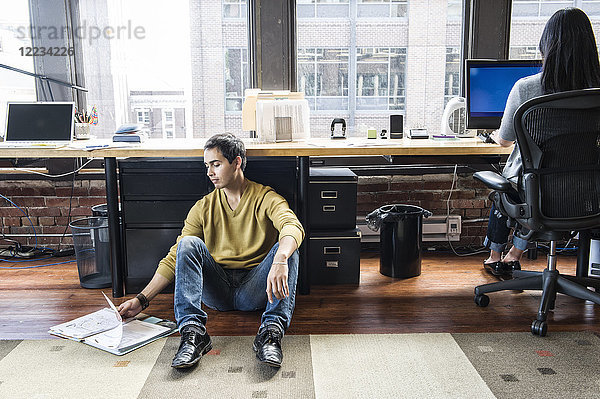 Lateinamerikanischer Mann  der auf einem Bodennetz zu seinem Arbeitsplatz in einem kreativen Büro sitzt.
