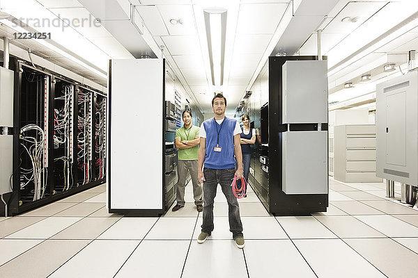 Portrait von drei multiethnischen Technikern  die in einem großen Computer-Serverraum arbeiten.