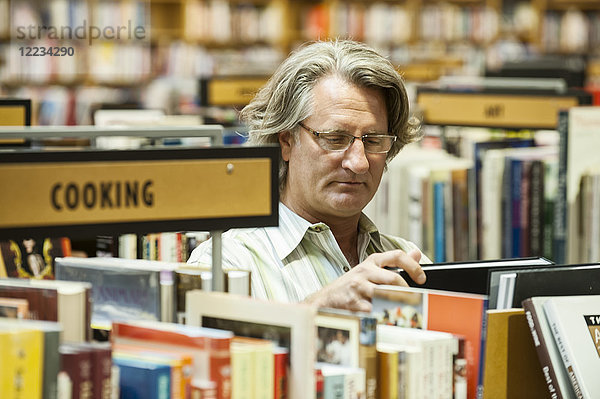 Kaukasischer Mann blättert in einer großen Buchhandlung in Büchern.