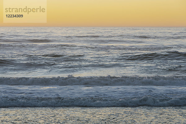 Meereslandschaft mit brechenden Wellen unter bewölktem Himmel bei Sonnenuntergang.