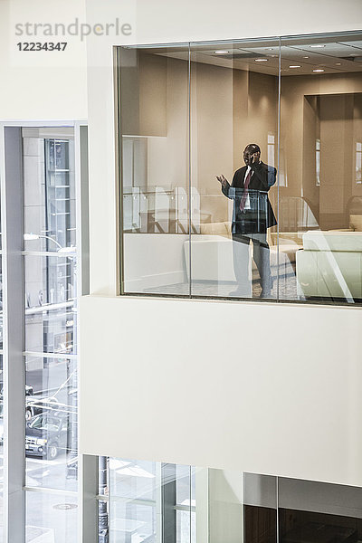 Schwarzer Geschäftsmann am Telefon  der am Fenster eines Konferenzraums steht.