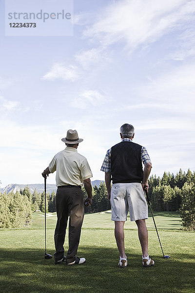 Von hinten betrachtet  schauen sich zwei ältere Golfer ein Fairway auf dem Golfplatz an.
