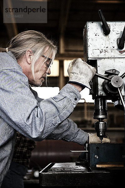 Kaukasischer Mann Fabrikarbeiter mit einer Bohrmaschine in einer Blechfabrik.