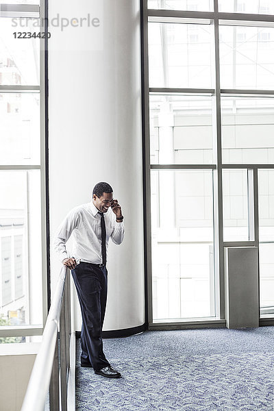 Schwarzer Geschäftsmann am Telefon in einer Büro-Lobby.