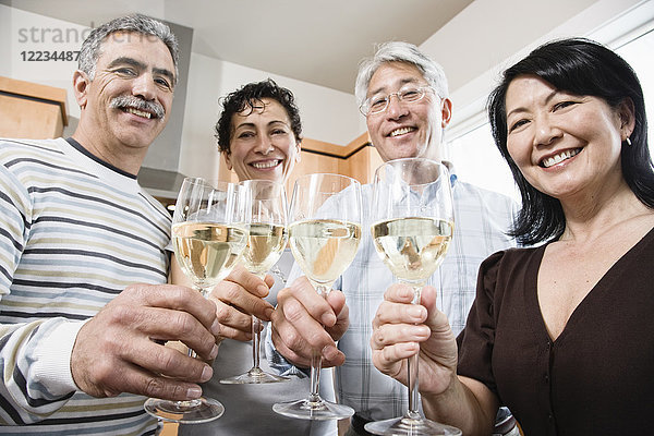 Zwei Paare in einer Küche  asiatische und kaukasische Männer und Frauen  die mit Gläsern Weißwein anstoßen.