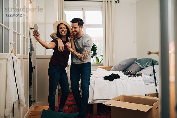 Smiling couple taking selfie on mobile phone while standing in bedroom