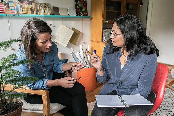 Female colleagues discussing over book while sitting in home office