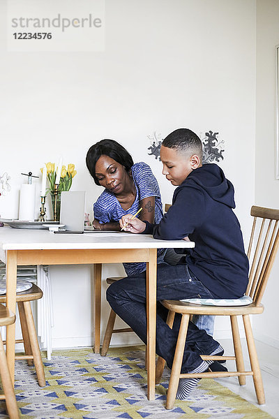 Mutter hilft Sohn bei den Hausaufgaben am Esstisch